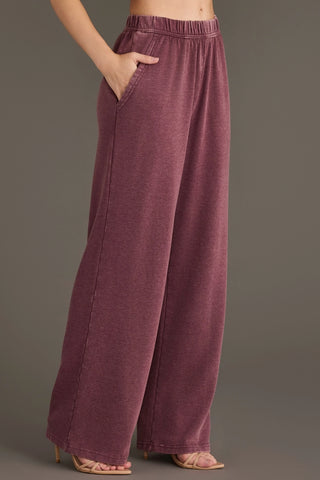 A person wearing wide-leg, high-waisted lounge pants in a heathered dusty rose or mauve color, paired with nude heeled sandals against a solid gray studio background.