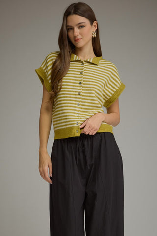 A woman modeling a short-sleeve knit polo shirt with horizontal lime green and white stripes, paired with black wide-leg trousers, against a solid gray studio background.